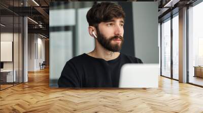 Image of serious man using wireless earphones and working with laptop Wall mural