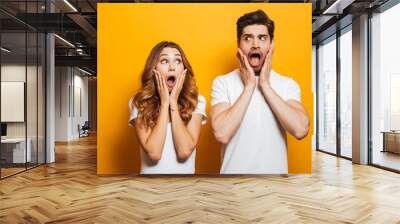 Image of shocked people man and woman in basic clothing expressing surprise or fright with open mouth covering face, isolated over yellow background Wall mural