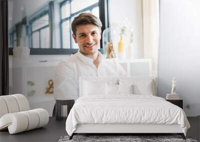 Image of smiling businesslike man sitting at table and working on computer in office Wall mural