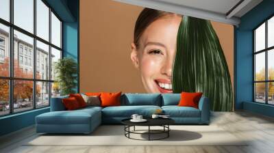 Image of smiling half-naked woman looking at camera and covering her face with green leaf Wall mural