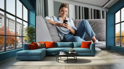 Image of smiling nice woman using cellphone while sitting on sofa Wall mural