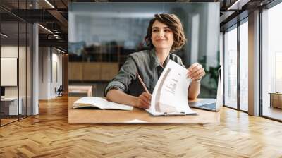 Image of smiling woman writing down notes while sitting at table Wall mural