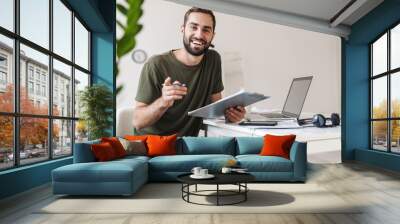 Image of smiling young man pointing finger at camera and holding clipboard Wall mural