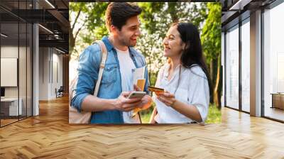 Image of student couple using mobile phone and holding credit card Wall mural