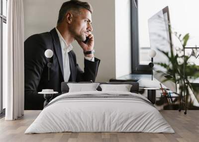 Image of successful businessman talking on cell phone while working on computer in office Wall mural