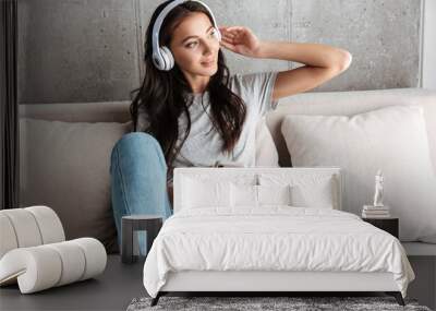 image of woman in headphones holding smartphone while sitting on sofa Wall mural