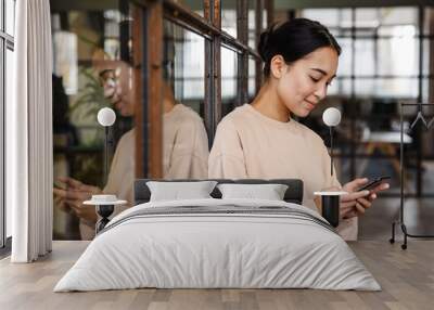 Image of young asian woman holding cellphone while working in office Wall mural