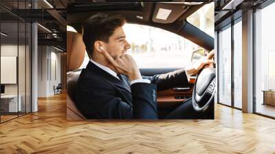 Image of young businesslike man in suit using earbuds while driving car Wall mural