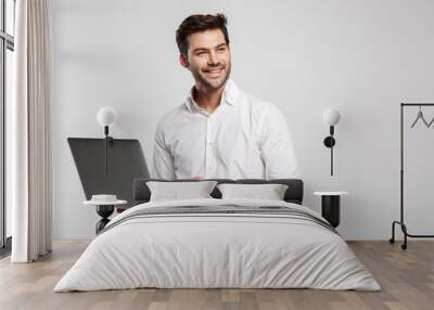 Image of young cheerful businessman holding and using laptop Wall mural