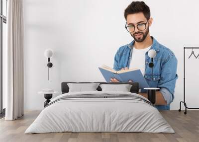 Image of young smart man wearing eyeglasses holding and reading book Wall mural