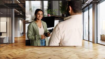 Indian business woman talking with her colleague while standing in office Wall mural