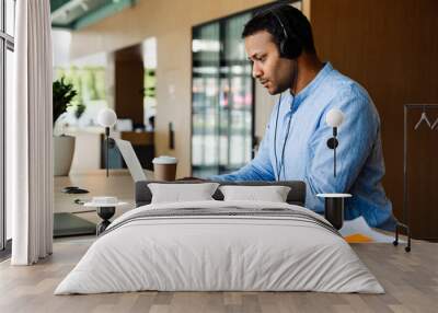 Indian businessman in headphones working on laptop computer in office Wall mural