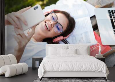 Lady listening music with headphones on copybooks using mobile phone. Wall mural