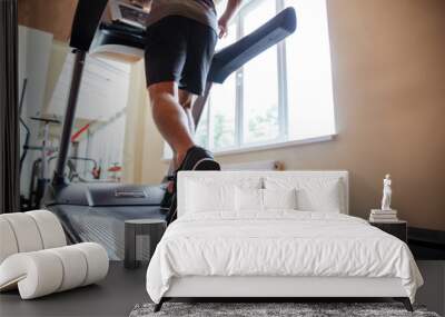 Legs of young man athlete running on treadmill in gym Wall mural