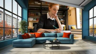 Lovely red haired teenage girl studying at the table Wall mural