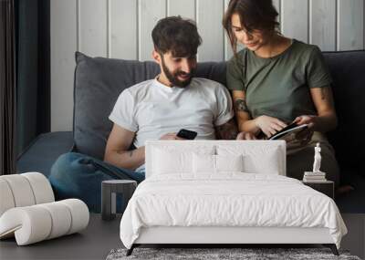 Lovely young couple relaxing on a couch at home, reading magazine Wall mural