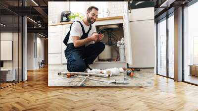 Man plumber work in uniform indoors using mobile phone. Wall mural