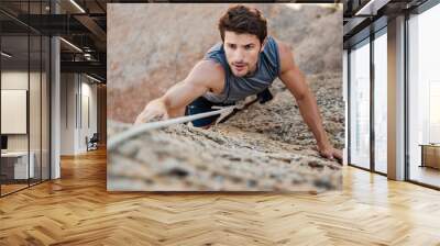 Man reaching for a grip while he rock climbs Wall mural