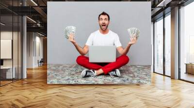 Man sitting on the floor with laptop and holding money Wall mural