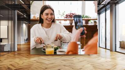 Man taking pictures of his girlfriend with mobile phone while having lunch together in cafe Wall mural