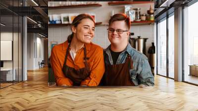 Man with down syndrome and his female colleague smiling while standing at counter in coffee shop Wall mural