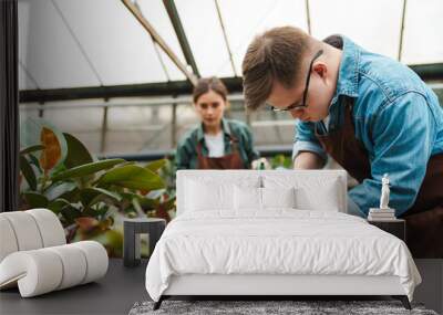 Man with down syndrome and woman gardener watering plants in greenhouse Wall mural