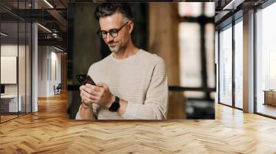 Middle-aged man using smartphone indoors Wall mural