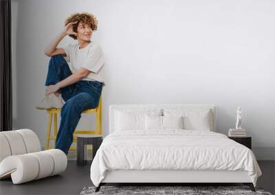 Middle-aged woman sitting on yellow chair and looking away at copy space isolated Wall mural