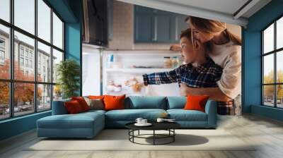 Mom hugging her son while standing together near fridge in kitchen Wall mural