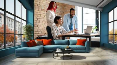 Multiracial smiling three colleagues talking and working with laptop Wall mural