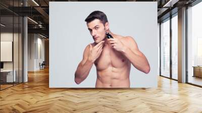 Muscular man shaving with electric razor Wall mural