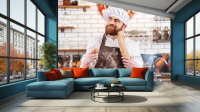 Pensive bearded baker holding eggs and bread on the kitchen Wall mural