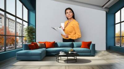 Pensive young businesswoman holding newspaper and cup of coffee Wall mural