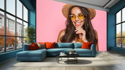 Photo closeup of european woman 20s wearing sunglasses and straw hat drinking juice from glass bottle, isolated over pink background Wall mural