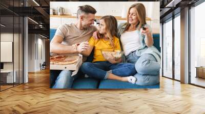 Photo of amusing family eating popcorn and pizza while watching tv Wall mural