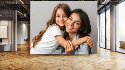 Photo of attractive woman with little daughter smiling and hugging together, isolated over gray background Wall mural