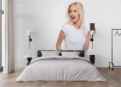 Photo of beautiful blonde woman with open mouth and hand in the pocket, showing blank smartphone screen Wall mural