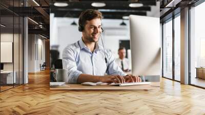 Photo of businesslike man 20s wearing office clothes and headset, working on computer in call center Wall mural