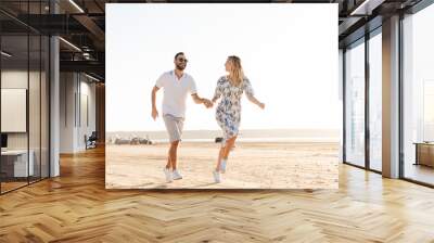 Photo of caucasian happy couple smiling and running on sunny beach Wall mural