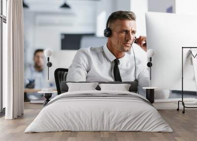 Photo of caucasian man 30s wearing office clothes and headset, sitting by computer in call center Wall mural