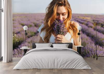 Photo of caucasian young woman in dress holding bouquet of flowers, while walking outdoor through lavender field in summer Wall mural