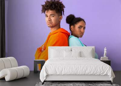 Photo of displeased african american couple in colorful clothes standing back to back, isolated over violet background Wall mural