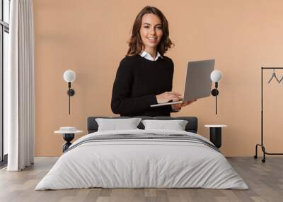 Photo of european woman 20s standing and holding laptop, isolated over beige background Wall mural