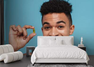 Photo of excited african american man showing vitamin capsule Wall mural