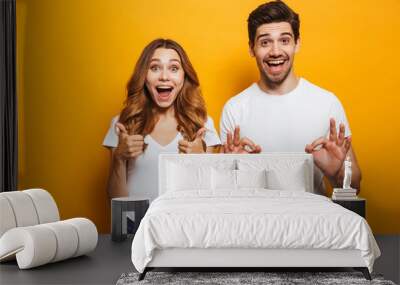 Photo of excited coup;e man and woman in basic clothing screaming and gesturing symbols with fingers at camera, isolated over yellow background Wall mural