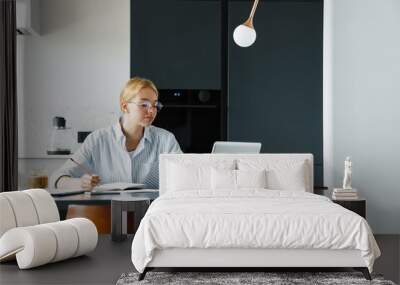 Photo of focused woman making down notes while working with laptop Wall mural