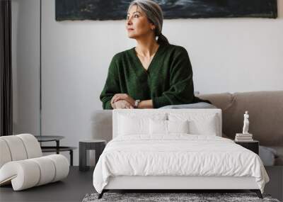 Photo of gray-haired focused woman looking aside while sitting on couch Wall mural