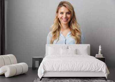 Photo of happy blond businesswoman with long curly hair smiling and standing with hands at pockets Wall mural