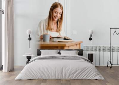 Photo of happy woman reading book while sitting at home kitchen Wall mural