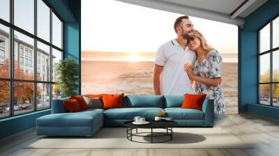 Photo of happy young couple smiling and hugging while walking on sunny beach Wall mural